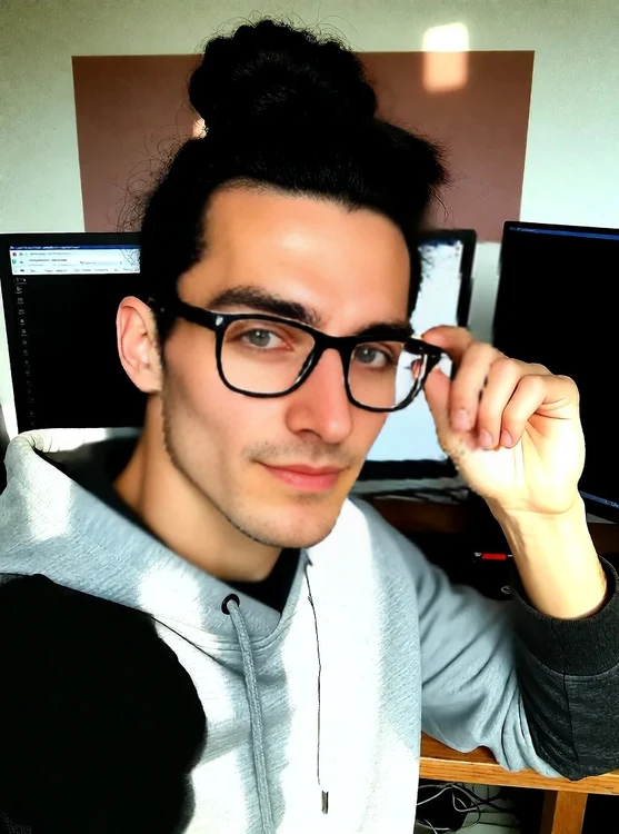 Finn - Selfie, Finn in gray hoodie at a desk with two monitors, adjusting glasses.